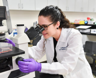 Doctor looking at a sample through a microscope at the Cancer Epigenetics Research Lab