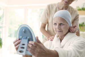 Nurse and patient with cancer wearing headscarf and looking at her reflection in the mirror.